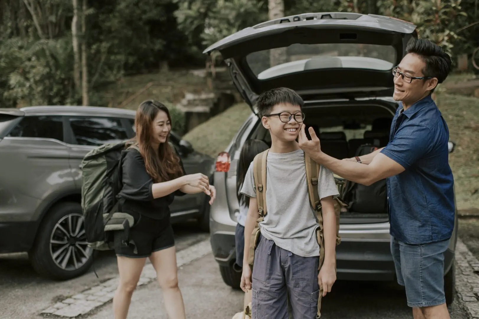 Father adjusts son's backpack while family loads car